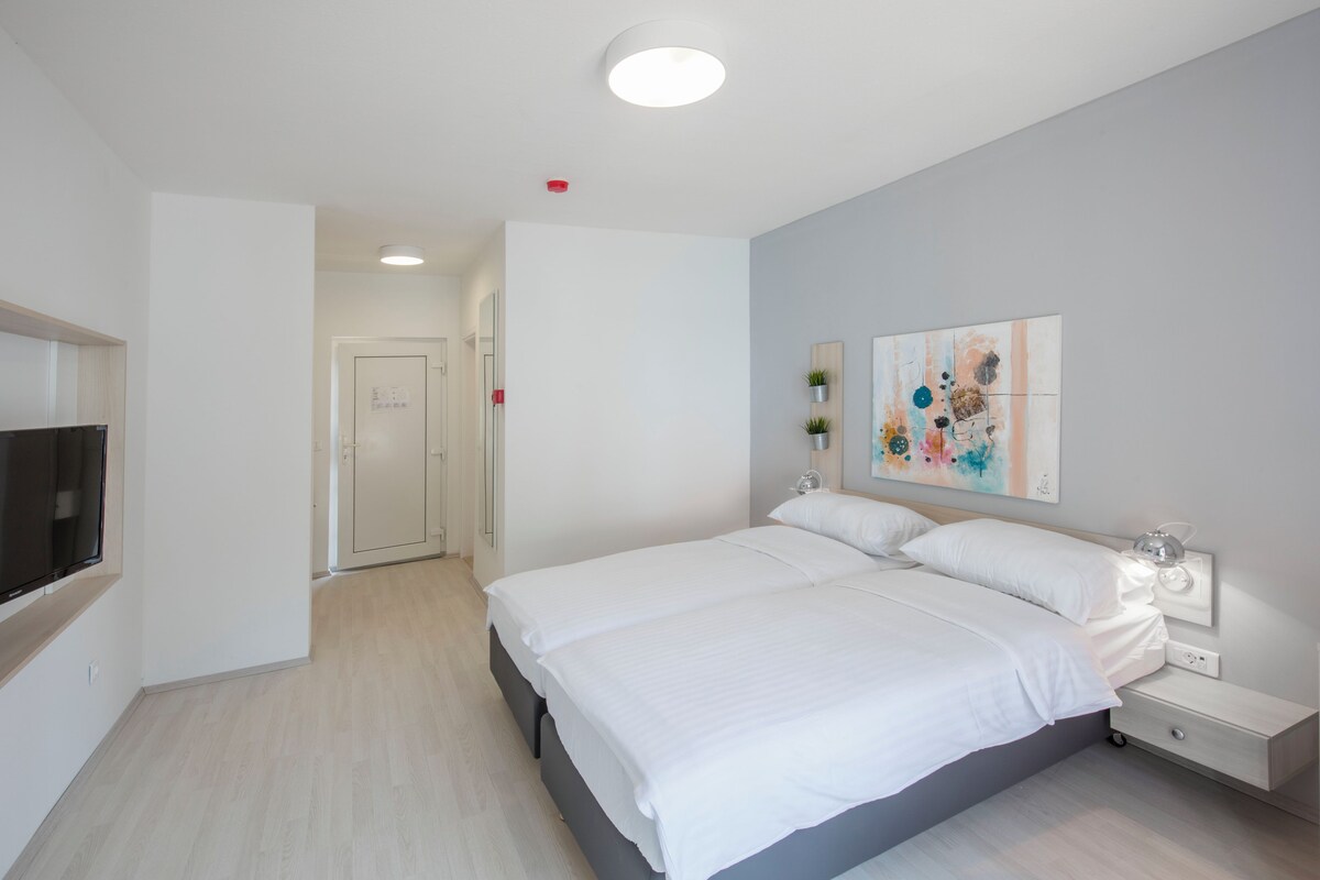 A modern bedroom with a large bed, bedside tables, a flat-screen TV, and a painting on the wall.