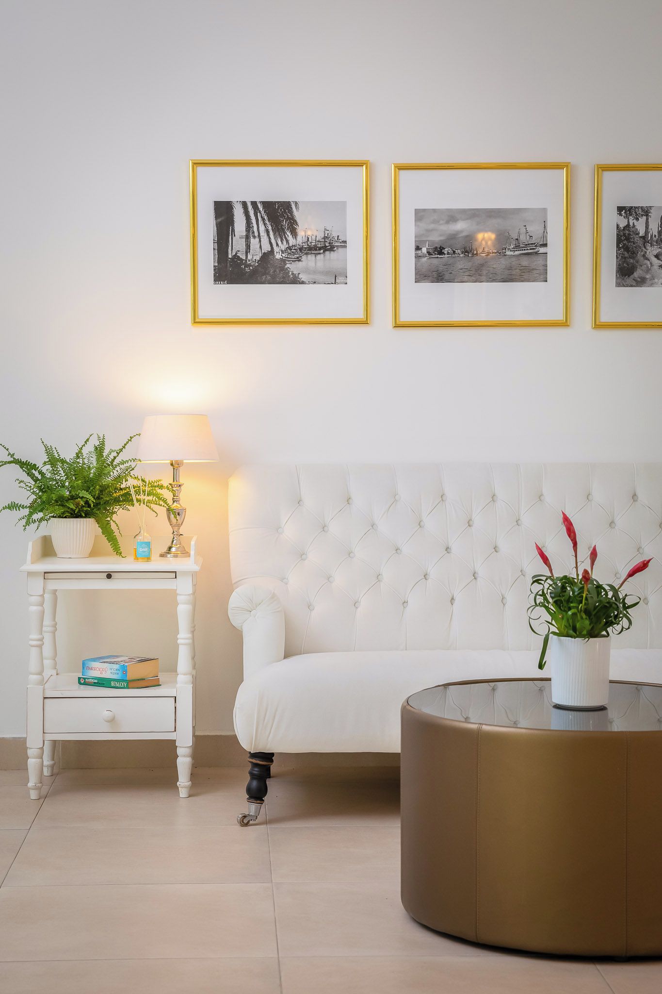 A living room with a white sofa, a round coffee table, a side table with a lamp, and three framed pictures on the wall.