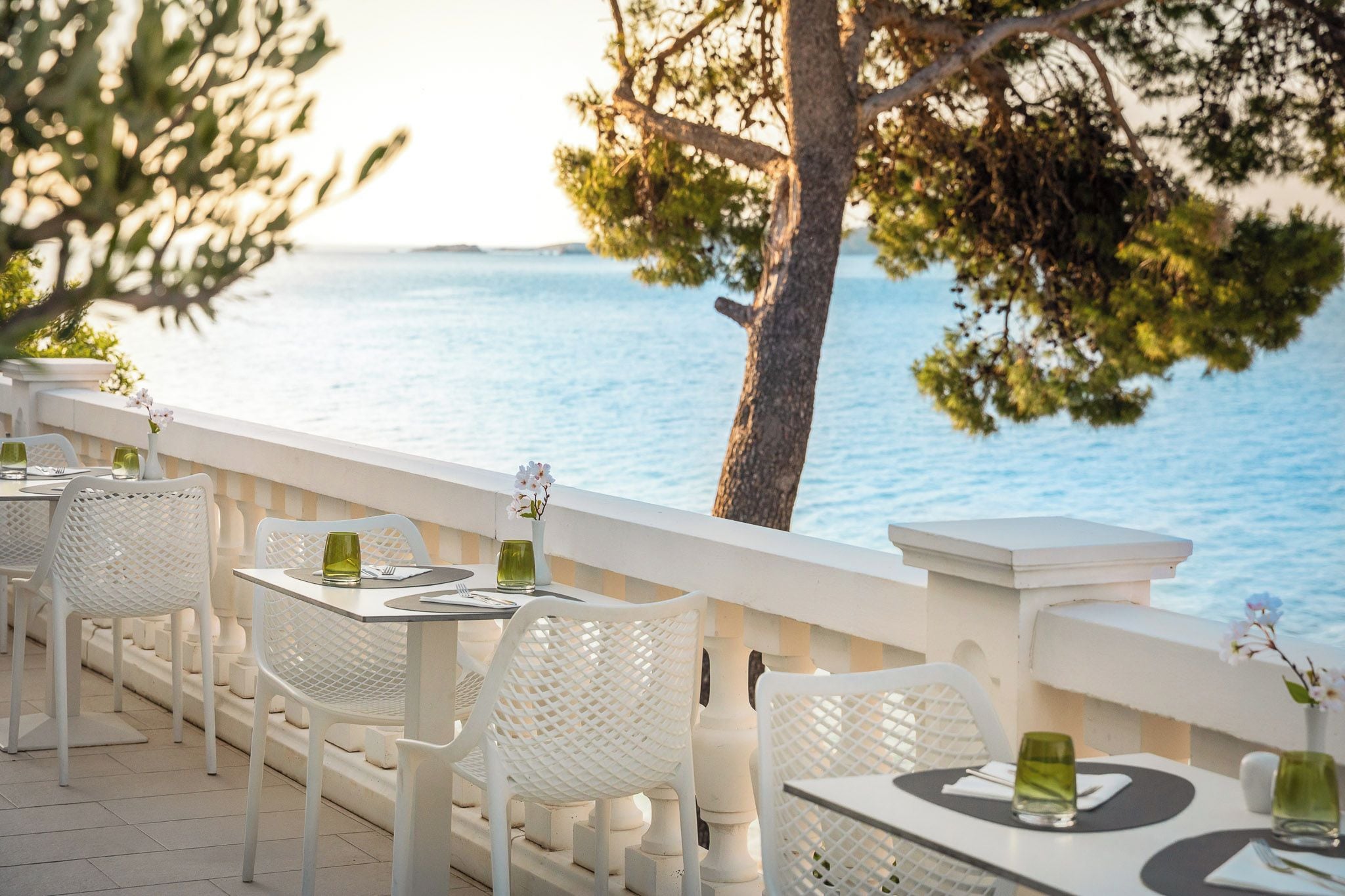 Un área de comedor al aire libre con sillas y mesas blancas, con vista a un cuerpo de agua.