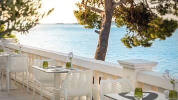 Un área de comedor al aire libre con sillas y mesas blancas, con vista a un cuerpo de agua.