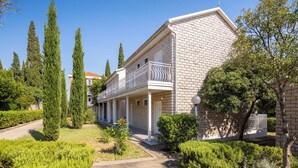 A two-story building with a brick facade, a balcony with a metal railing, and a well-maintained garden with various shrubs and trees. - Bellevue Maradiso Village by Aminess (Orebic)