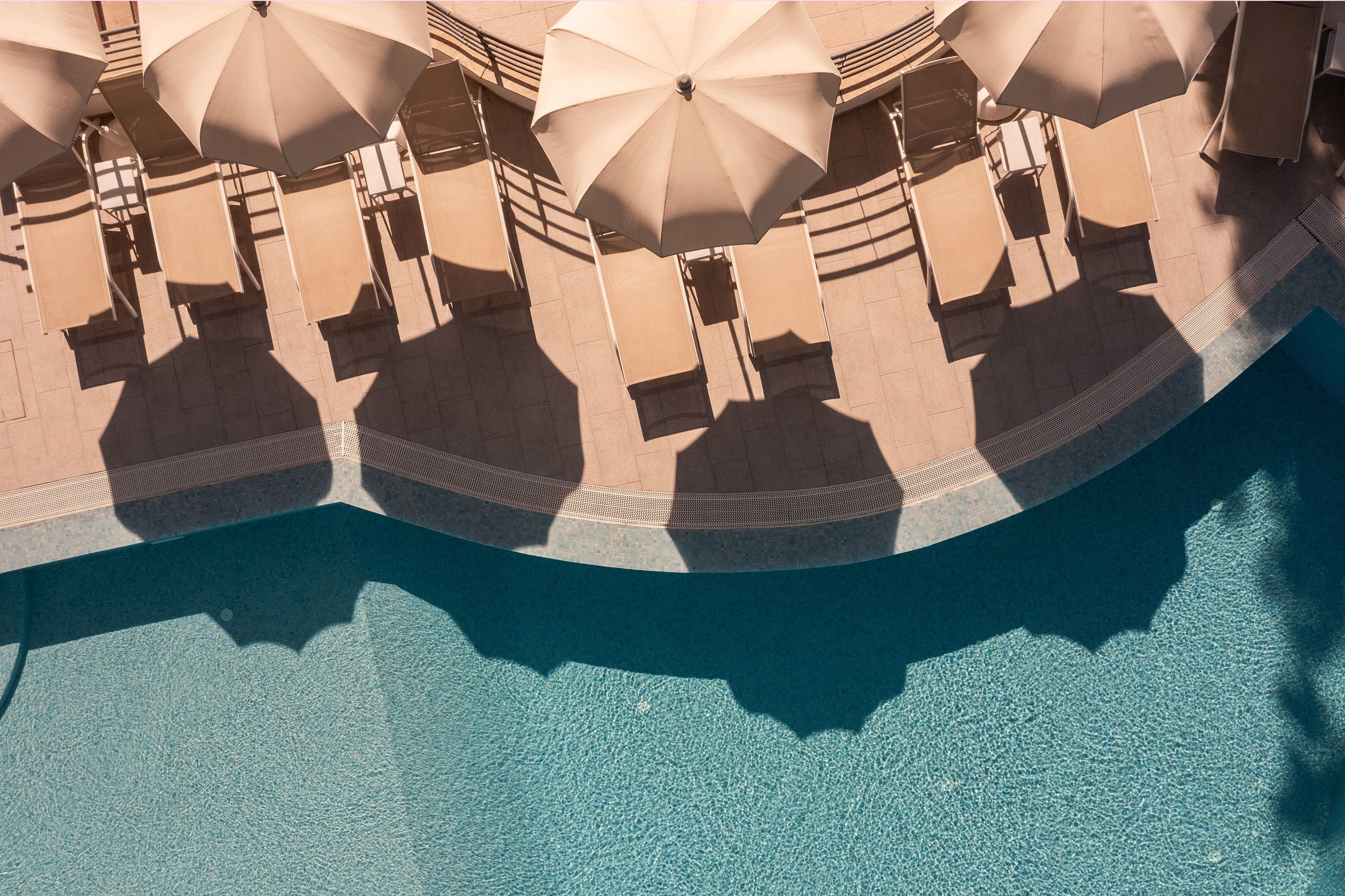 Un área junto a la piscina con varios sombrillas color beige y sillas de descanso.