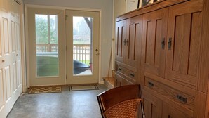 Ein Zimmer mit einer Schiebetür aus Glas, die zu einem überdachten Außenbereich führt, einem Holflanschrank mit mehreren Schubladen und einem Korbstuhl.