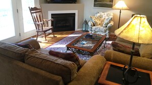 Ein Wohnzimmer mit Kamin, Fernseher, Sofa, Sessel und Lampe.