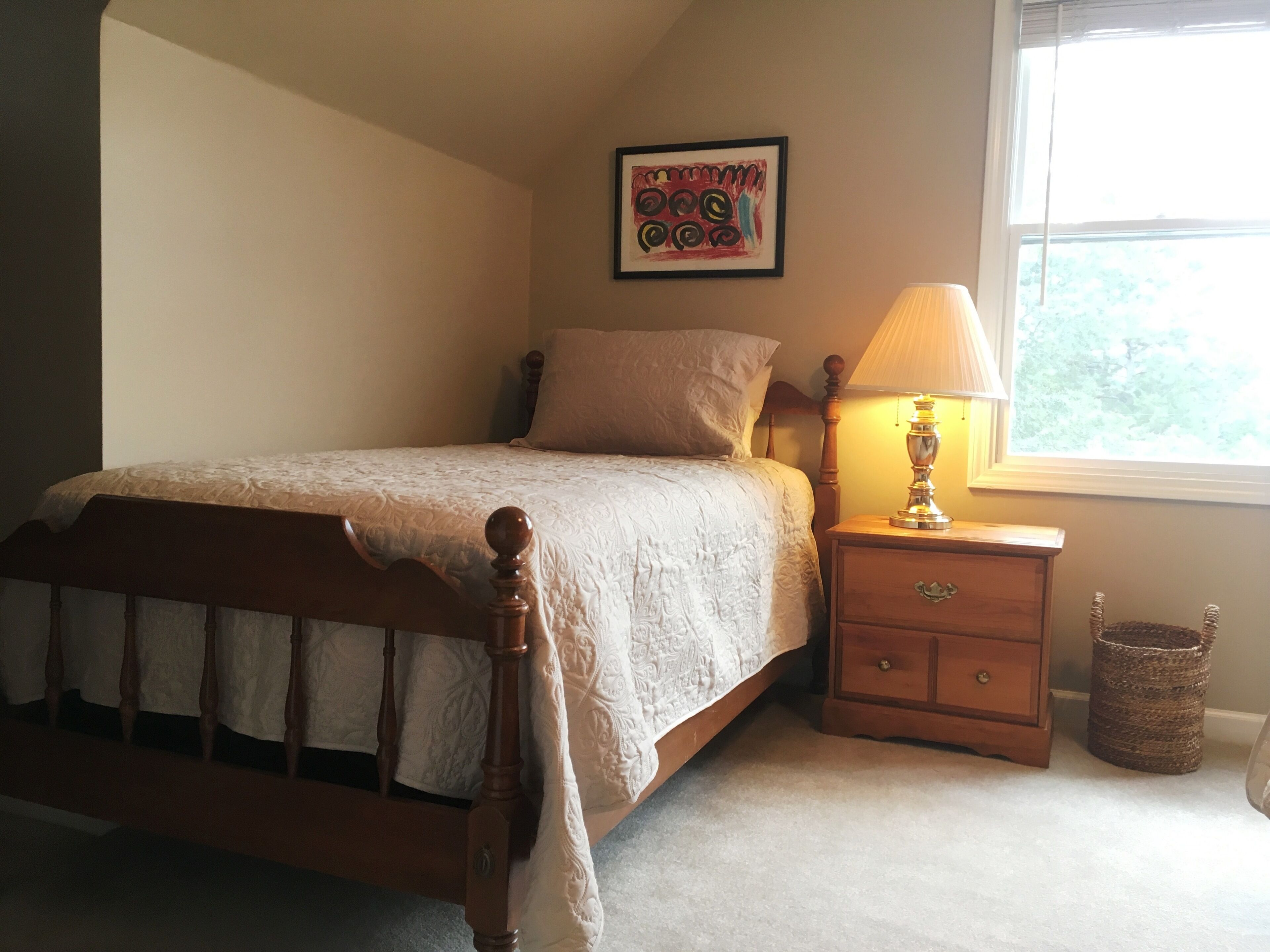 Une chambre à coucher avec un lit en bois, une table de chevet avec une lampe, un petit tiroir et un tableau encadré au mur.