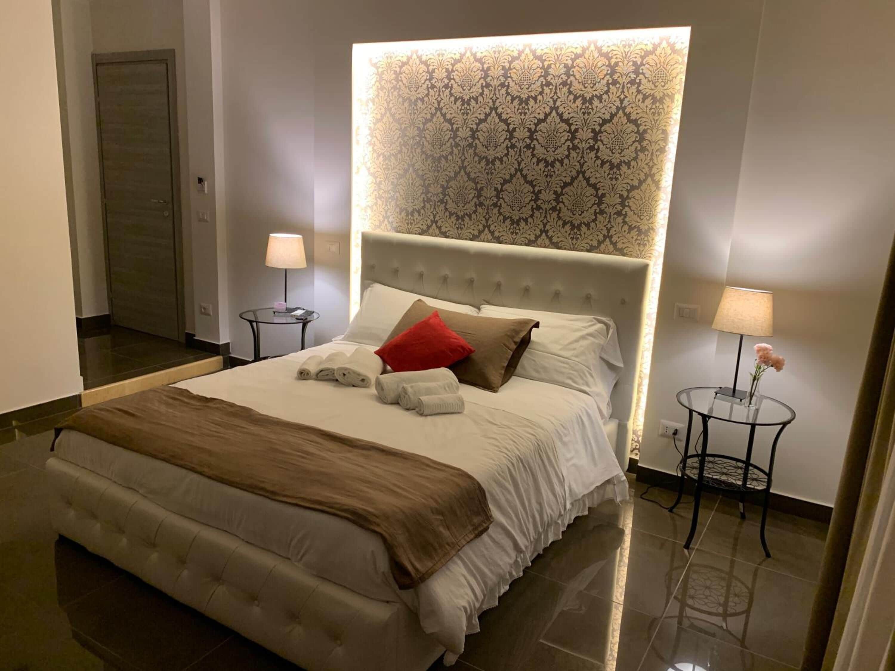 A hotel room with a large bed, two bedside tables, a round table, and a patterned wallpaper headboard.