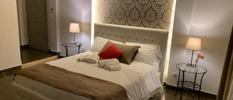 Habitación de hotel con una cama grande, dos mesitas de noche, una mesa redonda y un cabecero con papel tapiz estampado.