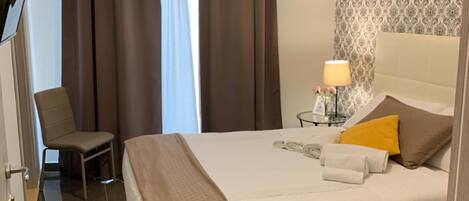 Una habitación de hotel con una cama, una silla, una mesita de noche con lámpara y un equipo de aire acondicionado.