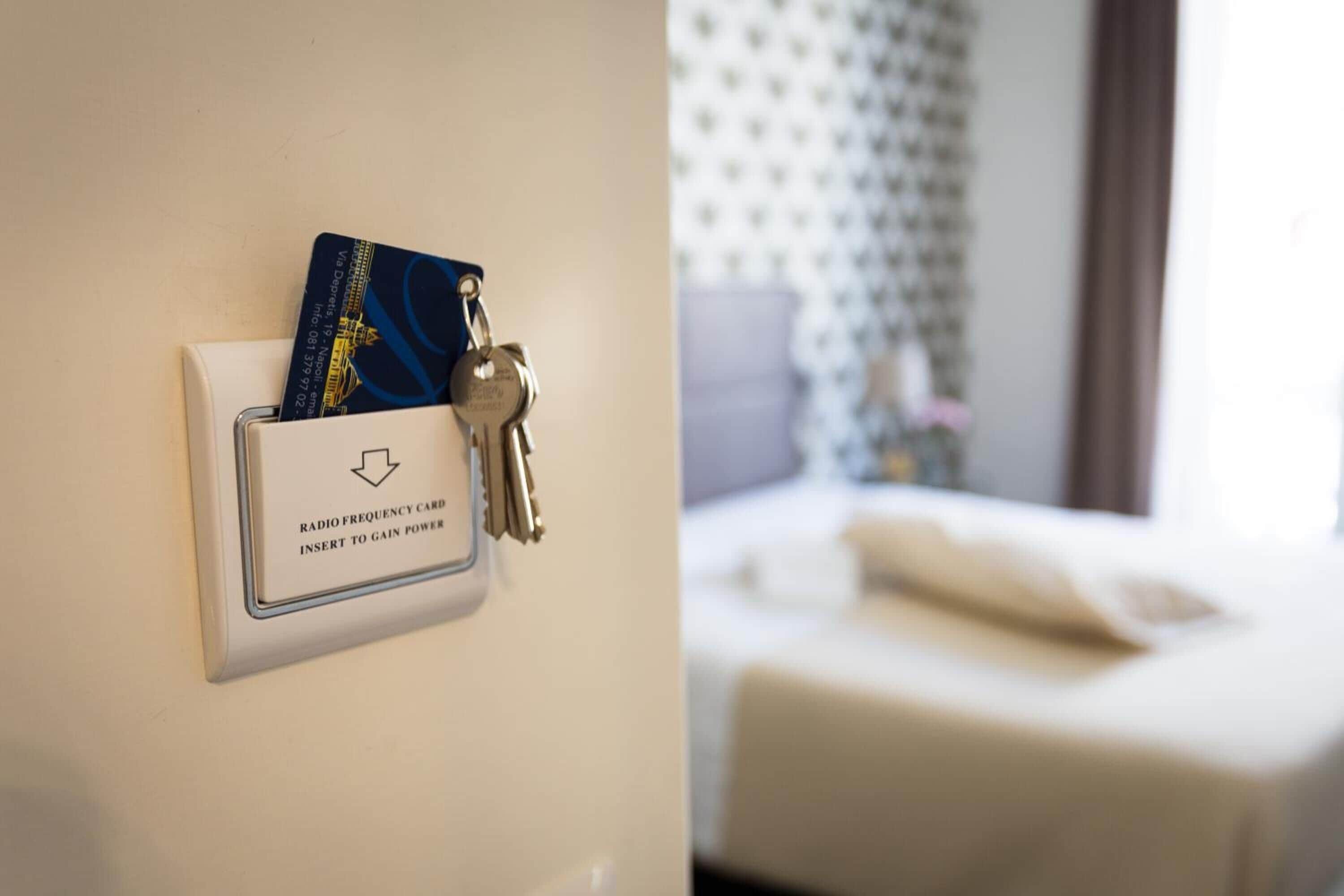 A hotel room with a bed, a nightstand, and a wall-mounted radio frequency card holder with keys.