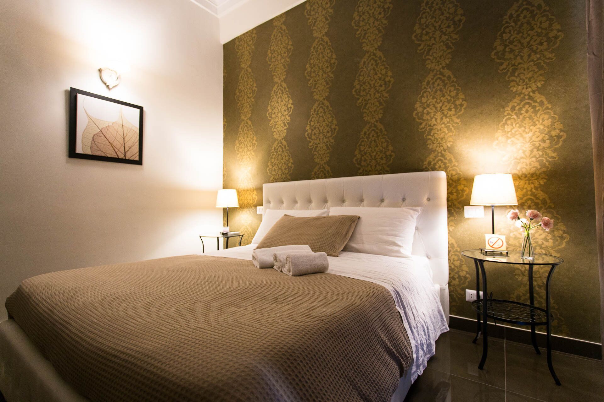 A neatly made bed with a white headboard, two bedside tables with lamps, and a framed picture on the wall.
