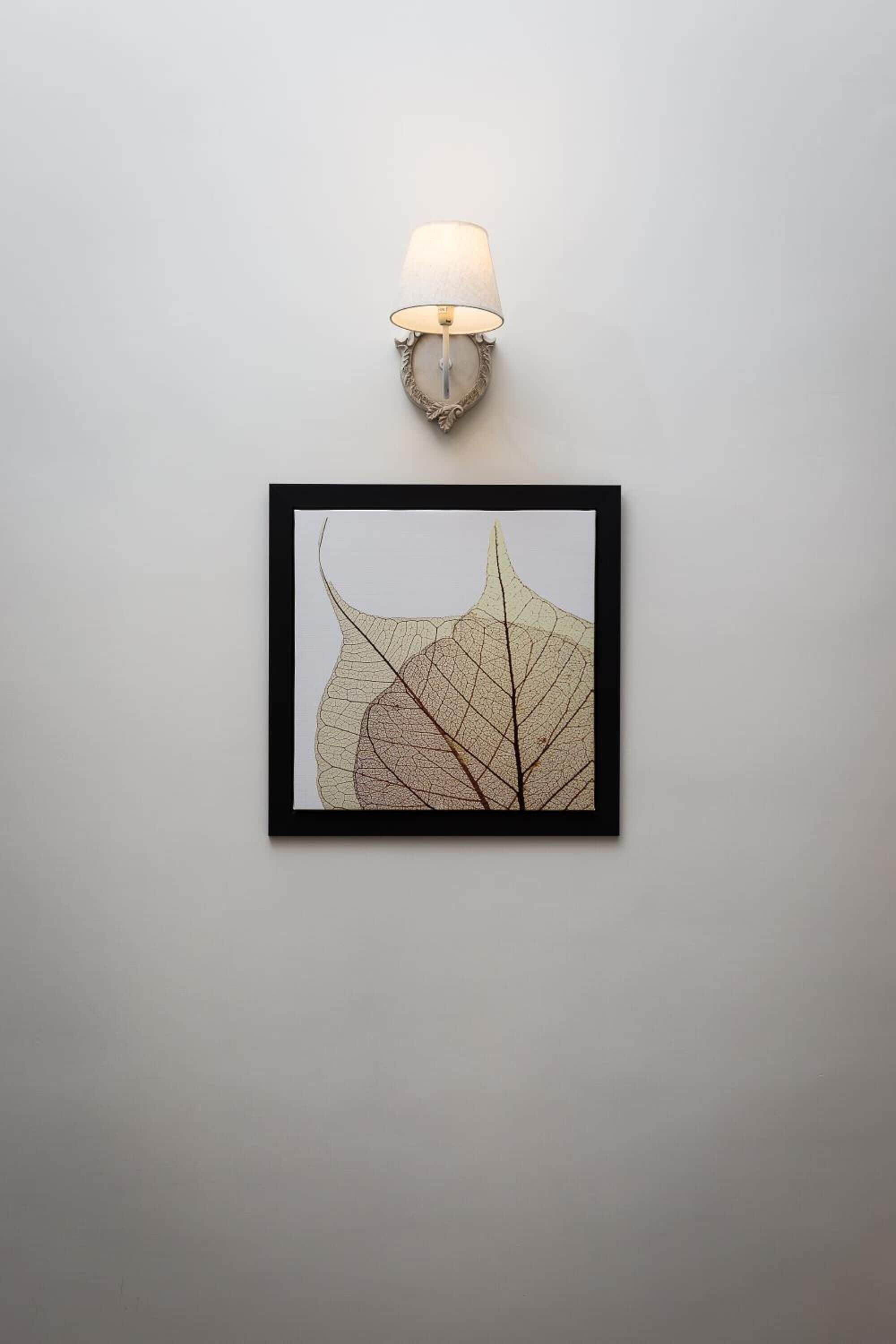 Ein gerahmtes Blattkunstwerk an einer Wand, darüber eine wandmontierte Lampe.