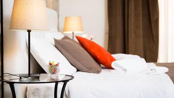 A neatly made bed with white and brown pillows, a glass table with a lamp, and a vase with flowers.