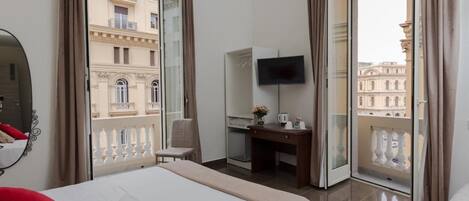 A hotel room with a bed, a desk, a TV, and a balcony with a view of buildings.