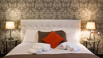 Un letto rifatto con cura, con copriletto marrone, cuscini bianchi e un cuscino decorativo arancione. Ci sono due comodini con lampade su entrambi i lati del letto.