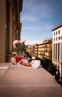 A balcony with a table set for a meal, including a croissant, a cup labeled "Caff. Beccucci," and a glass of red beverage.