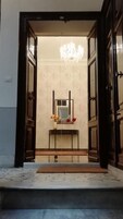 A hotel entrance with a chandelier, a mirror above a console table, and a doormat on the steps.