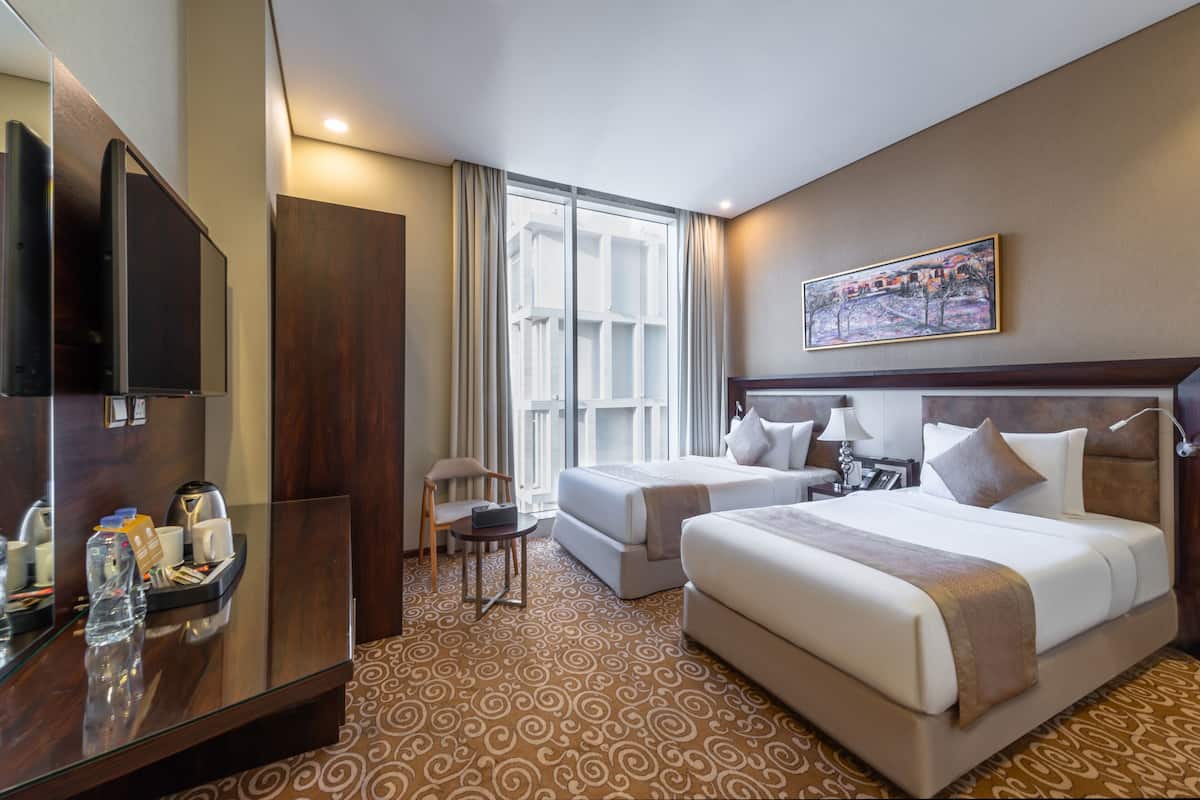 A hotel room with a large bed, a smaller bed, a desk with a TV, a chair, and a window with curtains.
