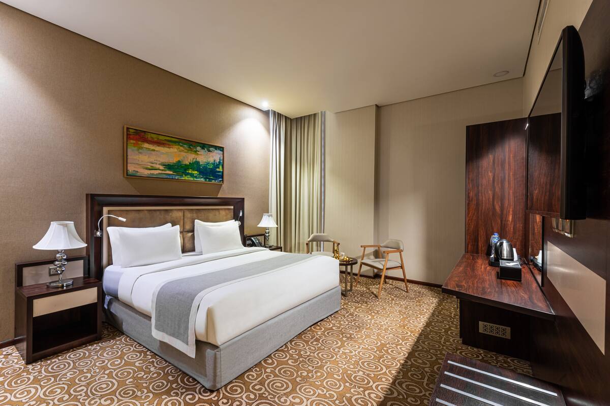 A hotel room with a large bed, a desk with a chair, a television, and a painting on the wall.