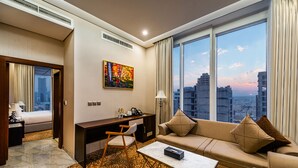 A hotel room with a large window, a sofa, a desk, and a chair. - Crowne Rose AlSahafa Hotel (Riyadh)