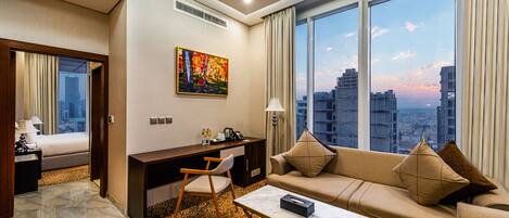 A hotel room with a large window, a sofa, a desk, and a chair.