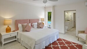 Een slaapkamer met een bed, nachtkastjes, een lamp, een plafondventilator, en een badkamer zichtbaar door een open deur, plus een rood tapijtend met een patroon.