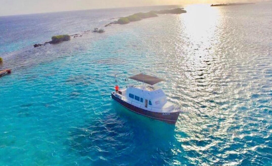 Een boot op helder turquoise water, met een rotsachtige kustlijn op de achtergrond.