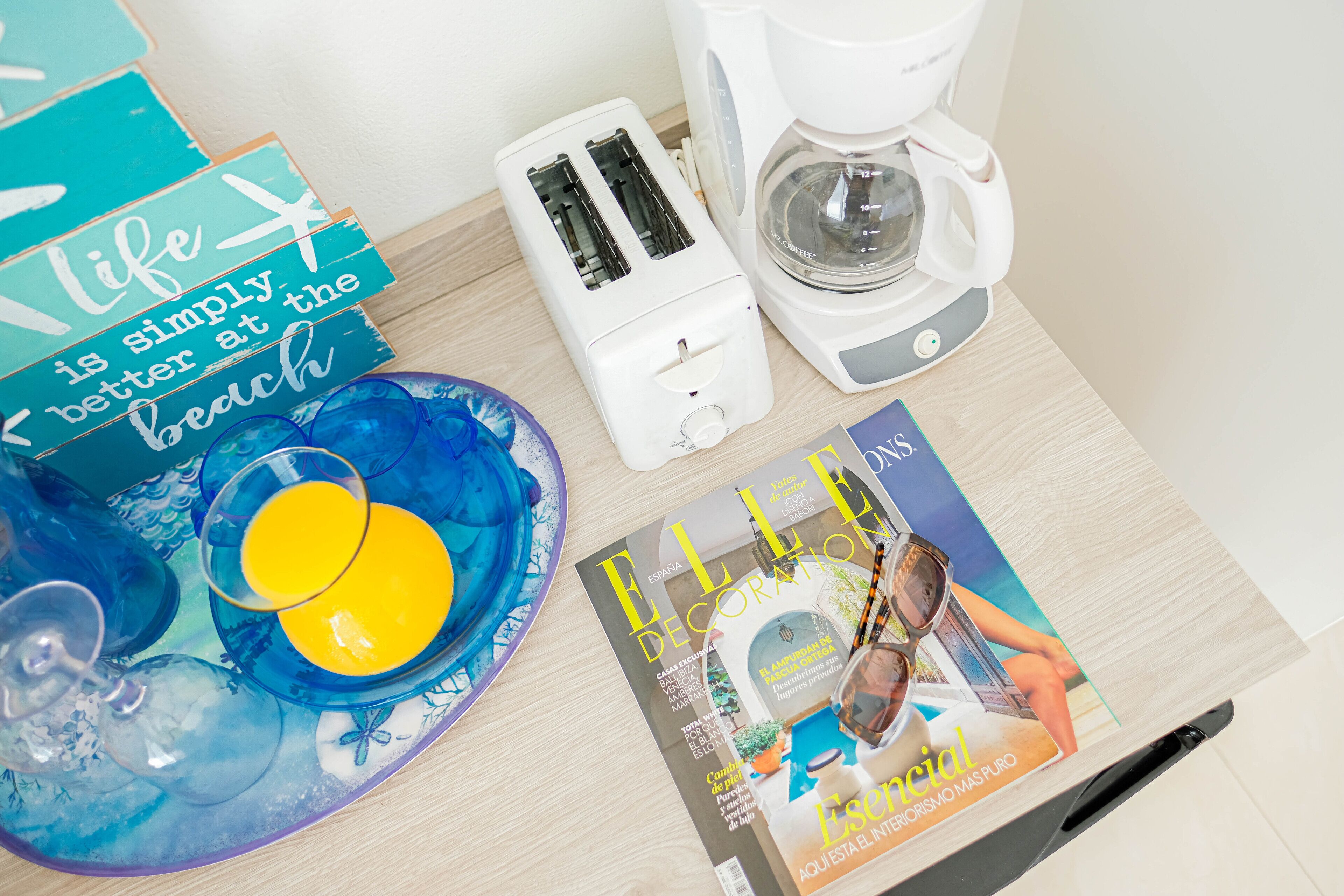 Una encimera de cocina con un tostador, una cafetera, una revista y un letrero decorativo.