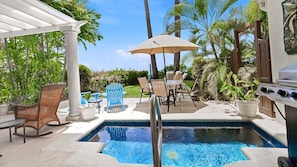 A pool area with a pergola, outdoor furniture, and a grill.