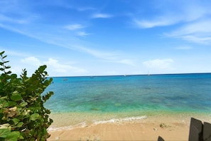 Een strand met helder turquoise water, een zandstrand en enkele boten in de verte.