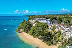 A coastal hotel with beach access, multiple-story buildings, and lush greenery.