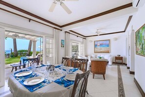 Un coin repas avec une table dressée pour six personnes, une chaise en osier et une vue sur l’océan.