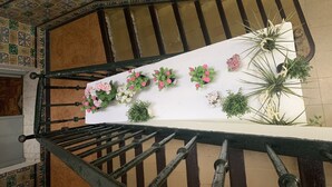 A staircase with a handrail, a white wall with potted plants, and a patterned ceiling. - Hostal Alcobia (Seville)