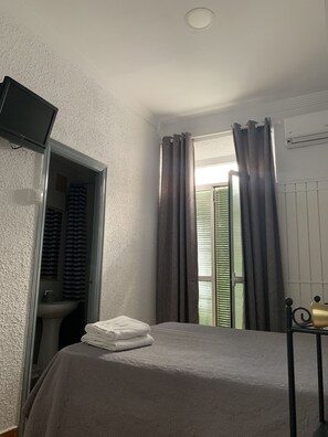 A bedroom with a bed, a television mounted on the wall, a window with curtains, and a radiator. - Hostal Alcobia (Seville)