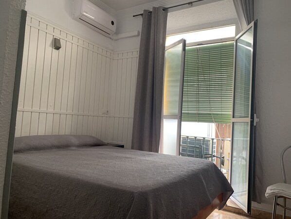 A bedroom with a bed, a window with blinds, and an air conditioning unit.