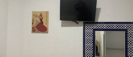 Quarto com televisão na parede, um cartaz decorativo e um espelho com moldura de azulejo azul.