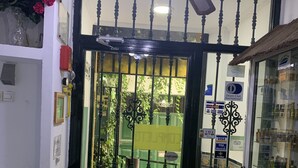 A hotel entrance with a decorative iron gate, a ceiling fan, and a glass display case with bottles. - Hostal Alcobia (Seville)