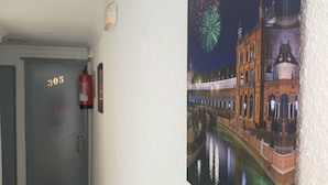 A hallway with a door labeled '305', a fire extinguisher, and a wall-mounted painting of a historic building with fireworks. - Hostal Alcobia (Seville)