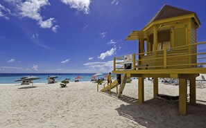Una torre de salvavidas en una playa con cielos despejados, sombrillas y sillas.