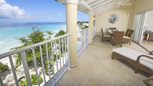Un balcon avec vue sur l’océan, des meubles en osier et un ventilateur de plafond.