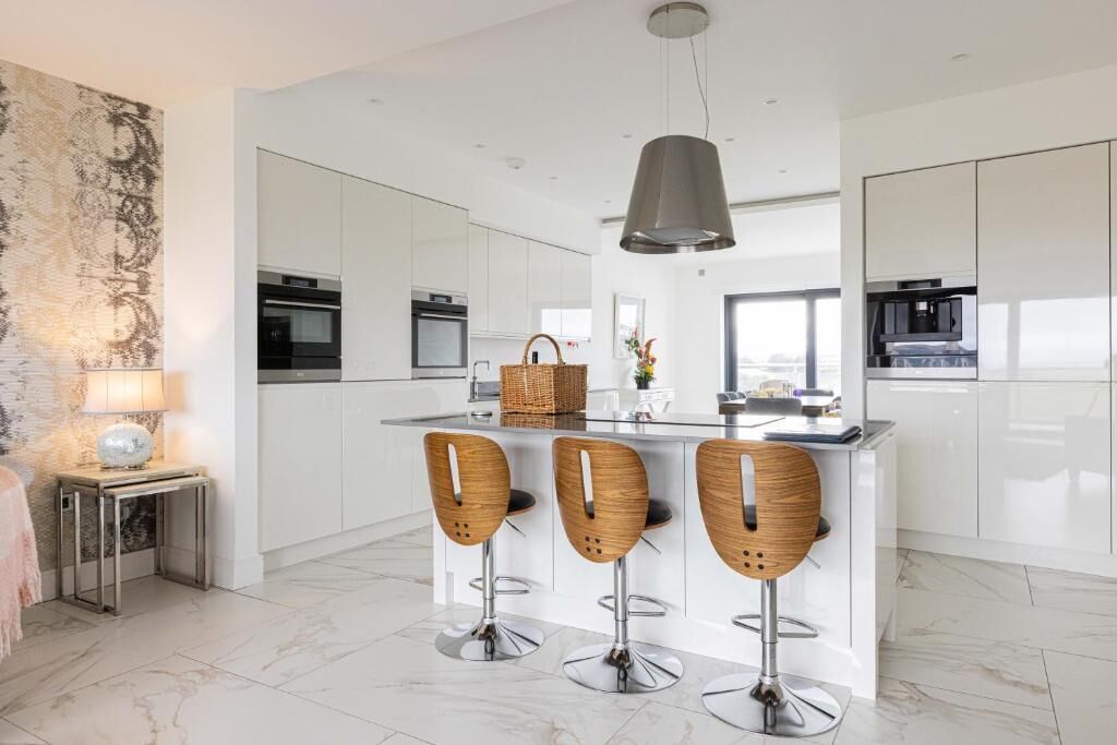 A modern kitchen with white cabinetry, a central island with bar stools, and a hanging light fixture.