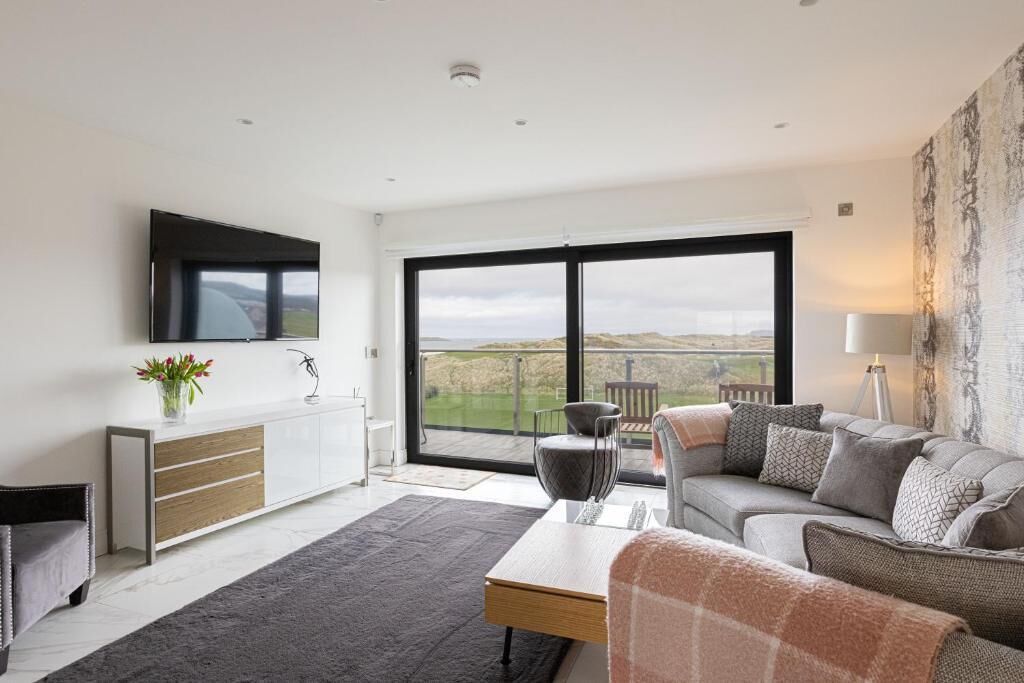 A modern living room with a large window, a flat-screen TV, a sofa, and a dining area.