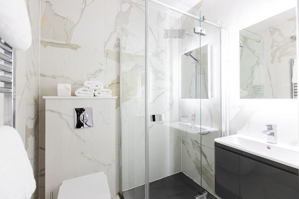 A modern bathroom with a glass shower enclosure, a white marble wall, a black cabinet, and a white sink.