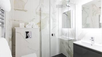 A modern bathroom with a glass shower enclosure, a white marble wall, a black cabinet, and a white sink.