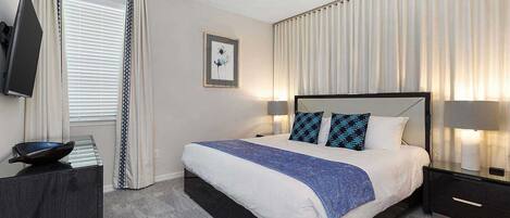 A modern hotel room with a large bed, a flat-screen TV, a ceiling fan, and a view of the city.