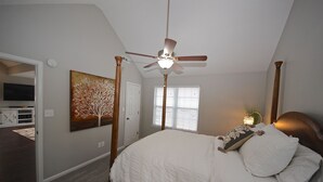 Un dormitorio con cama con dosel, ventilador de techo, pintura de un árbol y ventana con persianas.