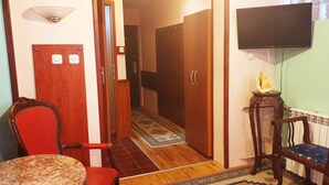 A room with a wooden door, a small table, a chair, a television mounted on the wall, and a radiator. - Hotel Kapistec (Skopje)