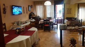 A dining area with multiple tables and chairs, a television mounted on the wall, and a wooden floor. - Hotel Kapistec (Skopje)
