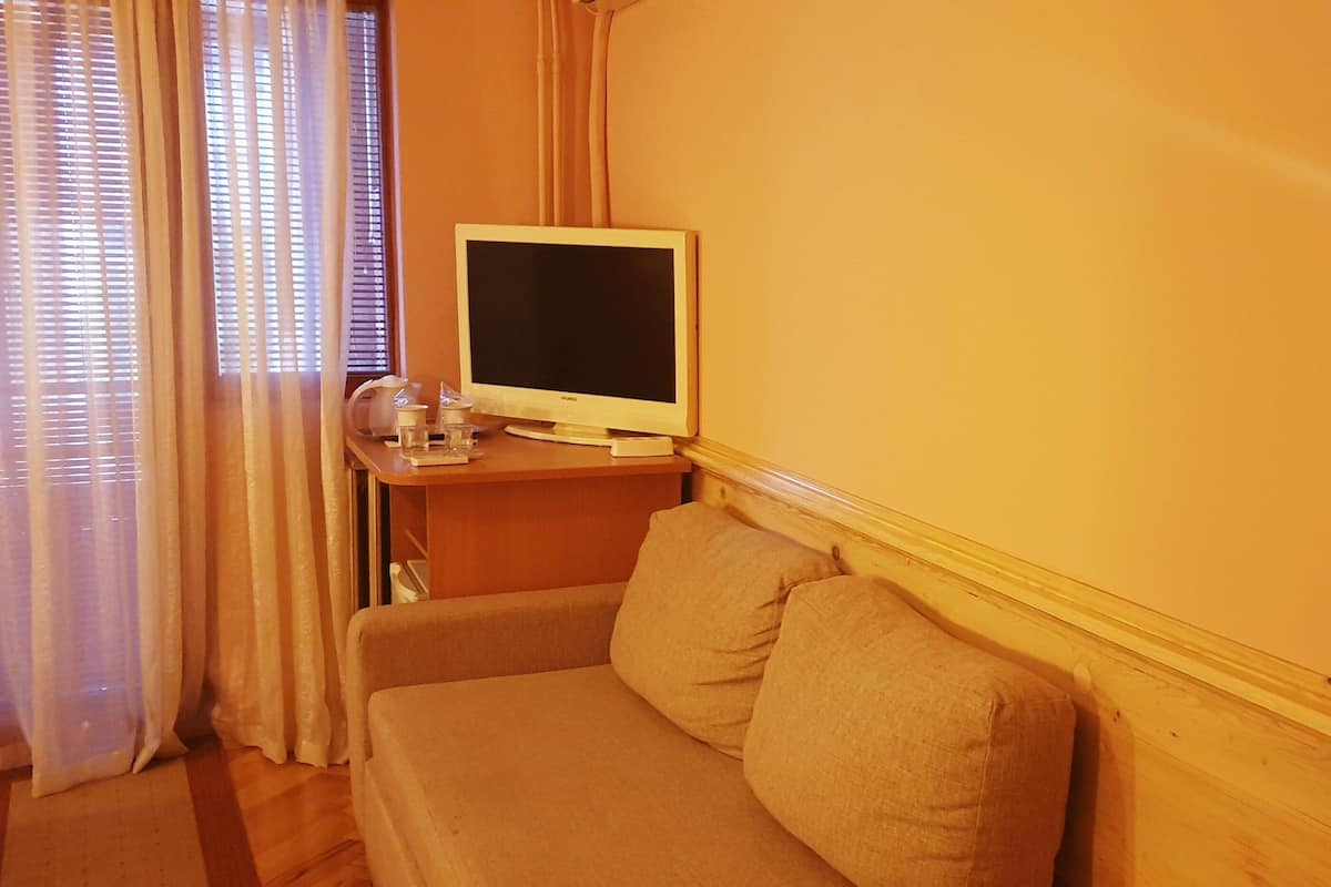 Una habitación de hotel con cama, sofá, televisión sobre una mesa de madera y una ventana con cortinas.