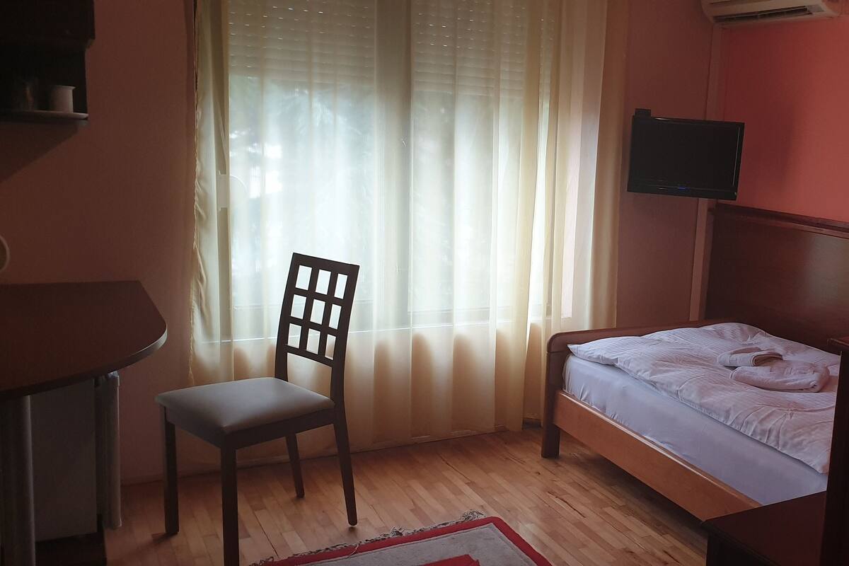 Una habitación pequeña con una cama individual, una silla, un escritorio y un televisor montado en la pared.