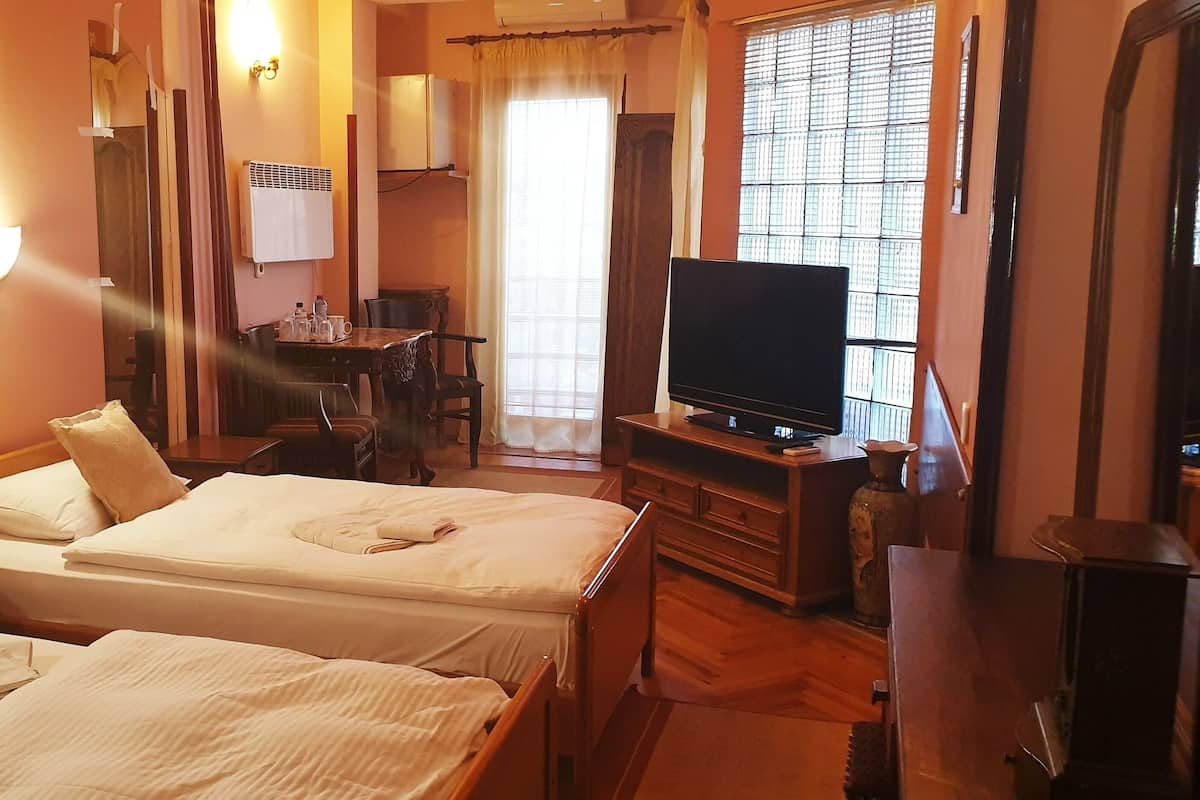 Una habitación de hotel con dos camas, un escritorio, un televisor y una ventana con persianas.